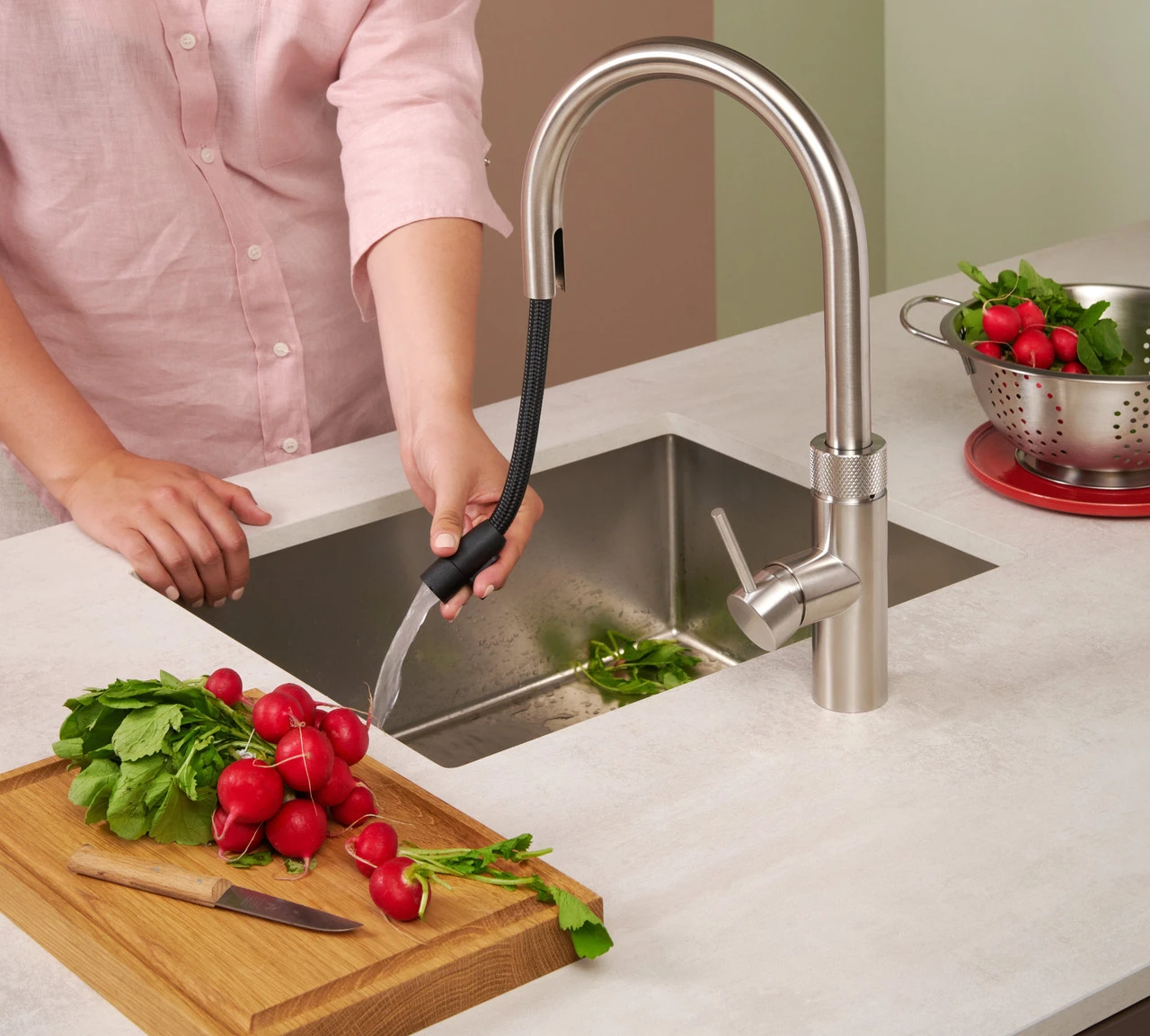 Brushed steel boiling water tap with pull-out spray hose rinsing radishes at a kitchen sink