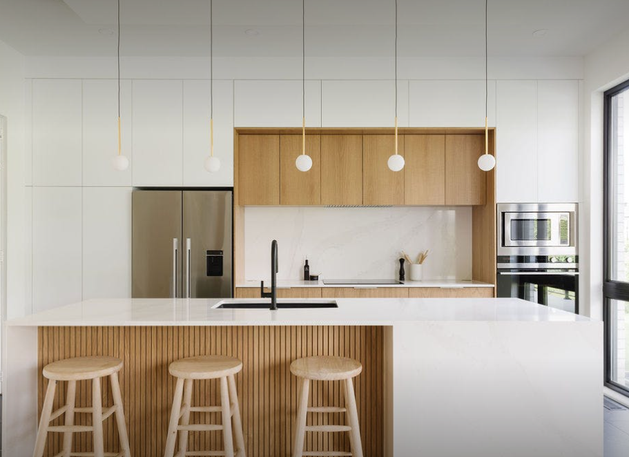 White Silestone island and worktop in a handleless kitchen with oak wall units