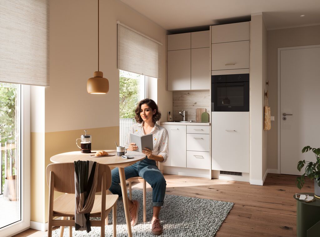 Impuls IP 2200 compact magnolia white kitchen in an open-plan apartment with a round dining table